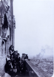 Les "Poules Grégoriennes" : femmes posant sur la galerie au dessous du bras sud du transept de la cathédrale de Reims : vue de l'est de Reims en arrière-plan.] / [abbé Thinot] | Thinot, Rémi (18..-1915) - abbé. Photographe