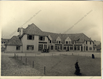 [Reims, Foyer Rémois, cité jardin du Chemin Vert, allée des Monts de Champagne : habitants posant devant le commerce "Les Etablissements Economiques"] / Photographie de Marcel Chrétien | Chrétien, Marcel. Photographe