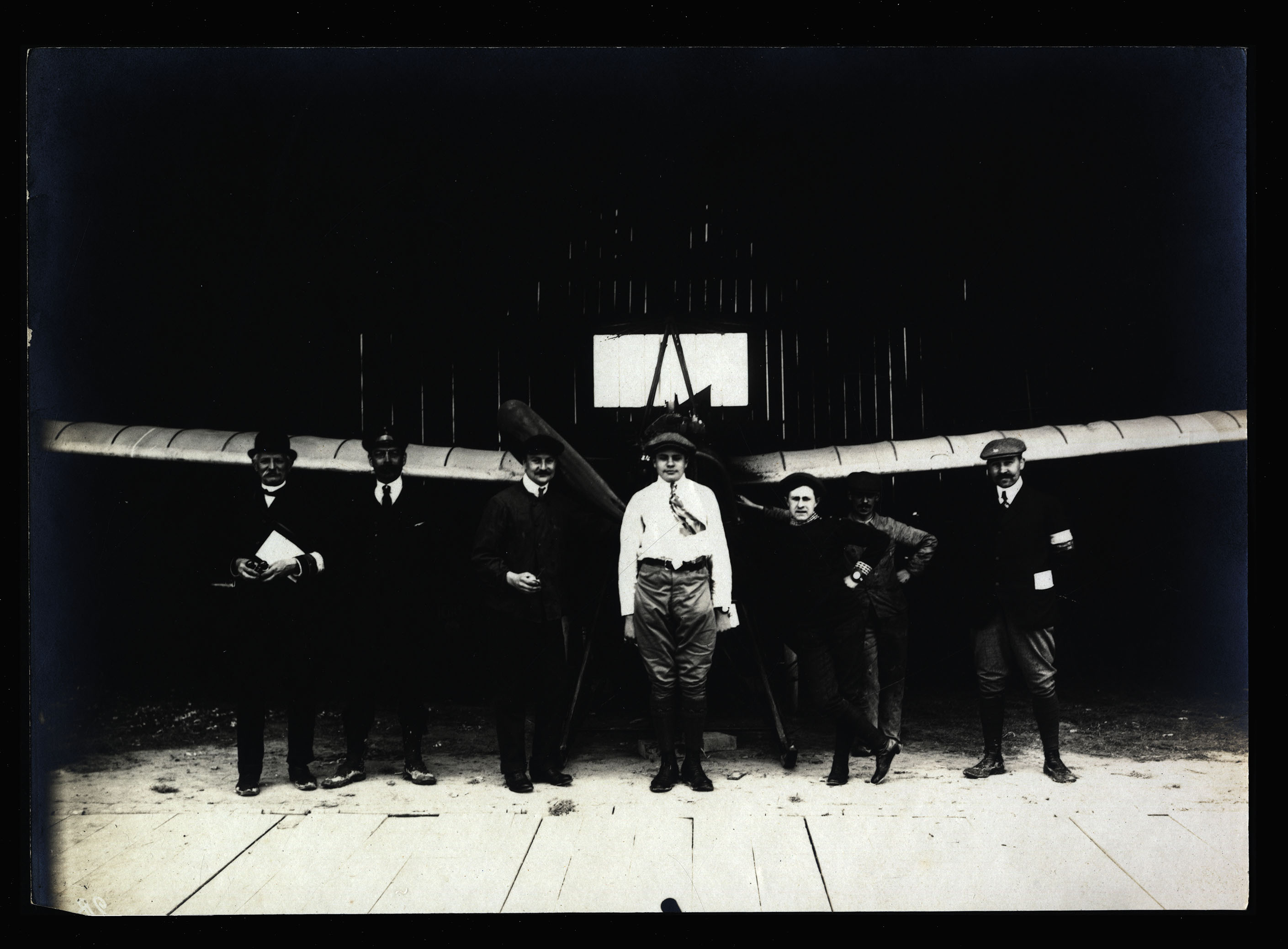 Grande semaine d’aviation 1909, Bétheny. Un pilote, son équipe et des juges à l’entrée d’un hangar devant un aéroplane "Antoinette". BM Reims, LX A 18.